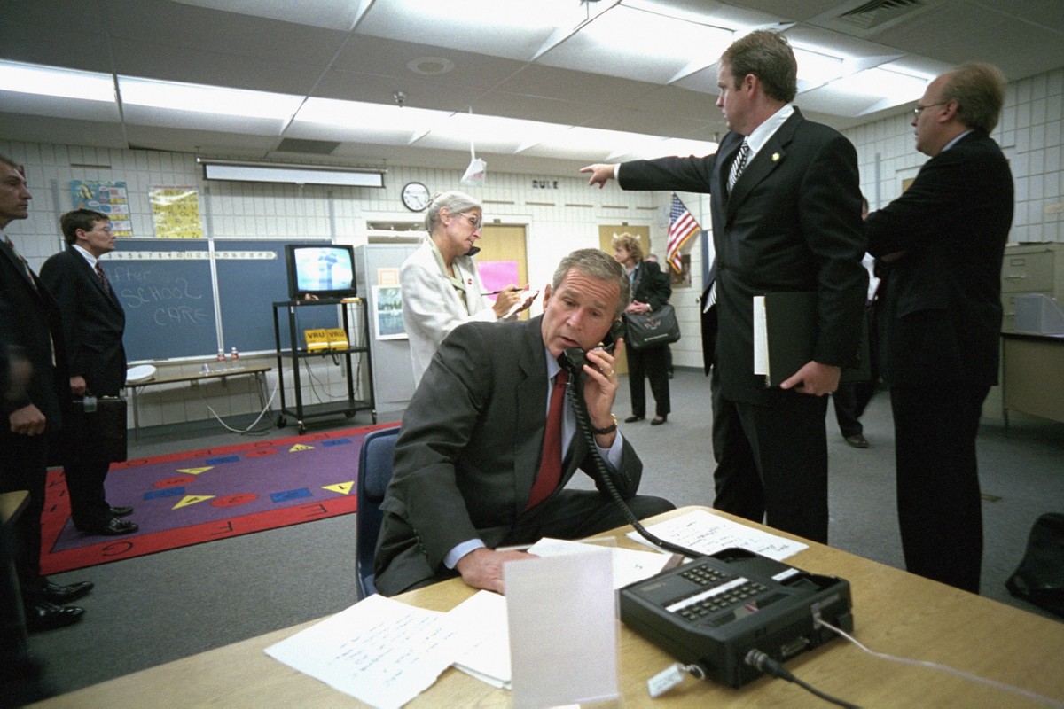 As Deputy Assistant Dan Bartlett points to news footage of the World Trade Center, President George W. Bush gathers information about the attack Tuesday, Sept. 11, 2001, from a classroom at Emma E. Booker Elementary School in Sarasota, Fla. Also pictured are Director of White House Situation Room Deborah Loewer, directly behind the President, and Senior Advisor Karl Rove, far right.  Photo by Eric Draper, Courtesy of the George W. Bush Presidential Library