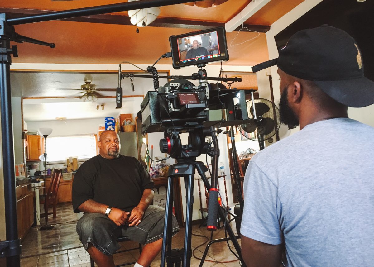 Image of Facing Life subject Melvin Smith sitting in his home being filmed by a large video camera visible in the foreground.