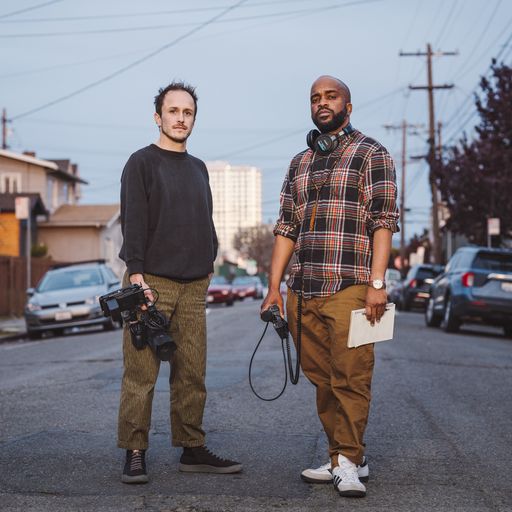 Image of Brandon Tauszik (left) and Pendarvis Harshaw (right). Tauszik is a white man wearing a black sweashirt and khakis; he holds a video camera. Harshaw is a black man wearing a plaid shirt and khakis. He holds a microphone and has headphones around his neck.