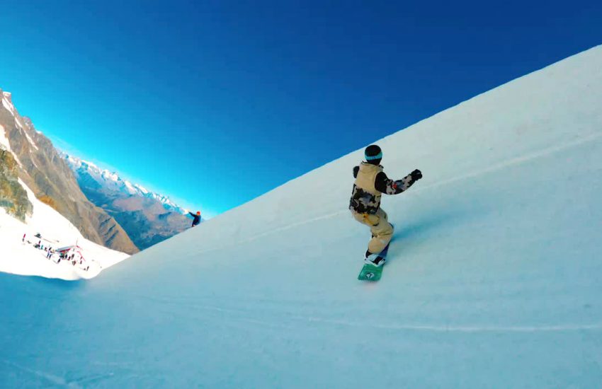 A snowboarder seen from behind as they navigate a steep course.