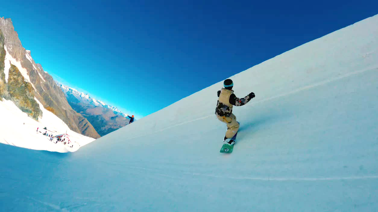 A snowboarder seen from behind as they navigate a steep course.