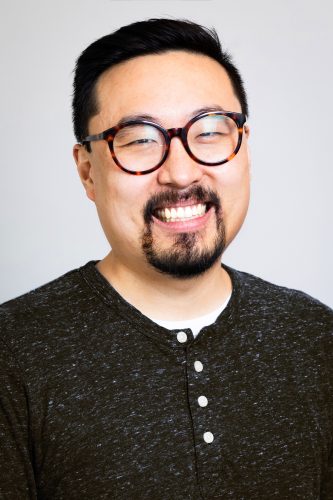 Chang poses for a headshot photo against a blank grey background.