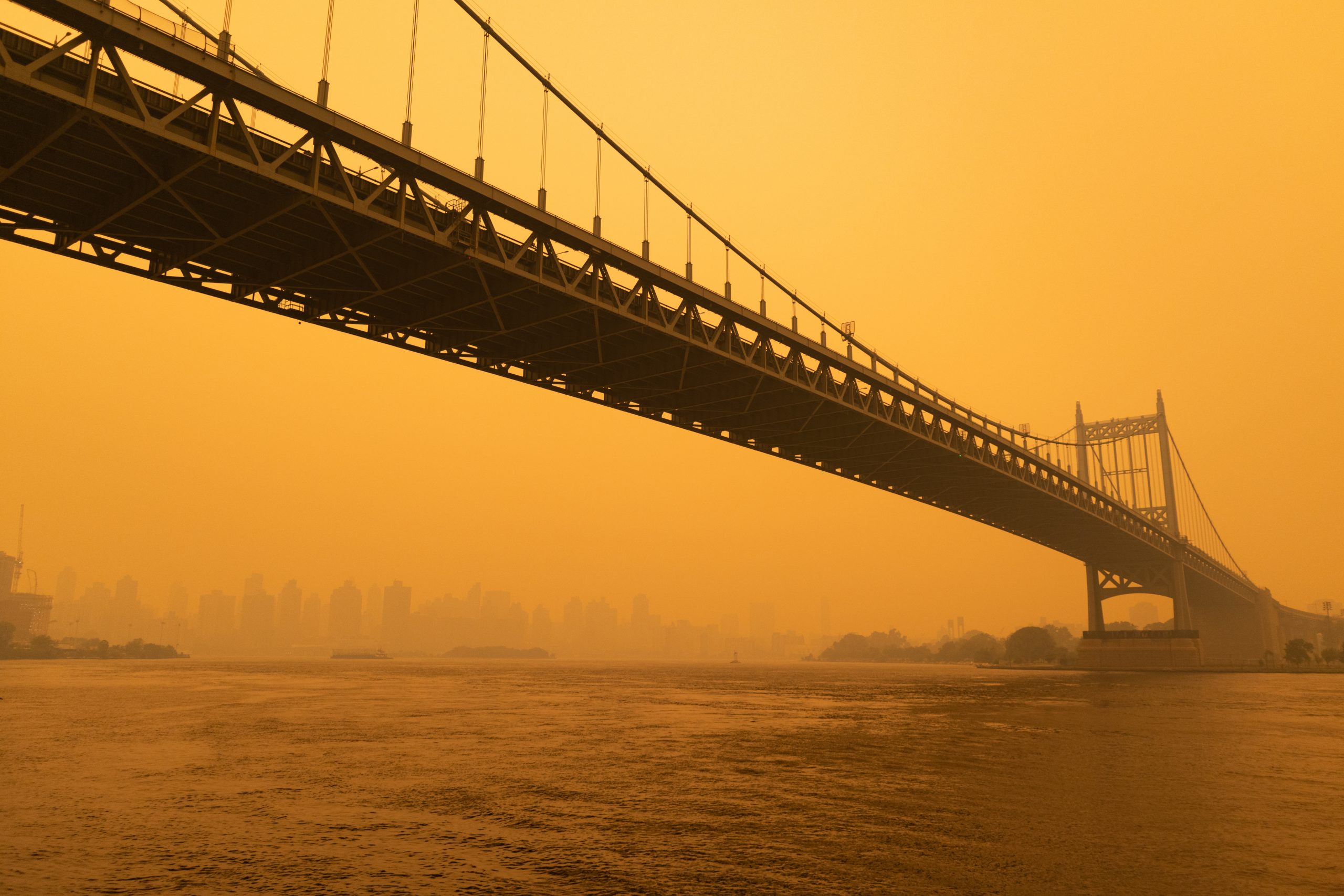 The Triborough Bridge crossing the East River shrouded in smoke from wildfires, The smoke has turned the daytime sky orange.