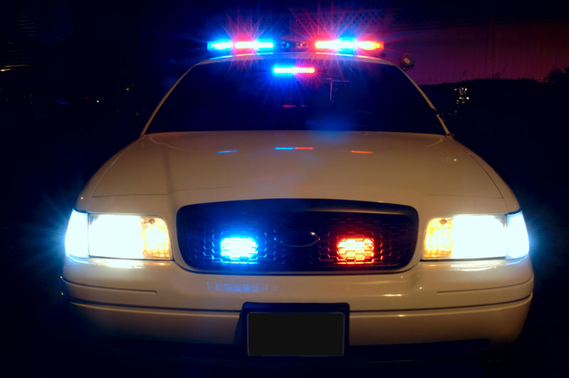 Photo shows a police car seen at night from the front with emergency lights flashing.