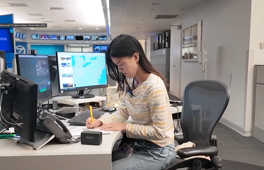 Photo shows woman in a newsroom writing at a desk