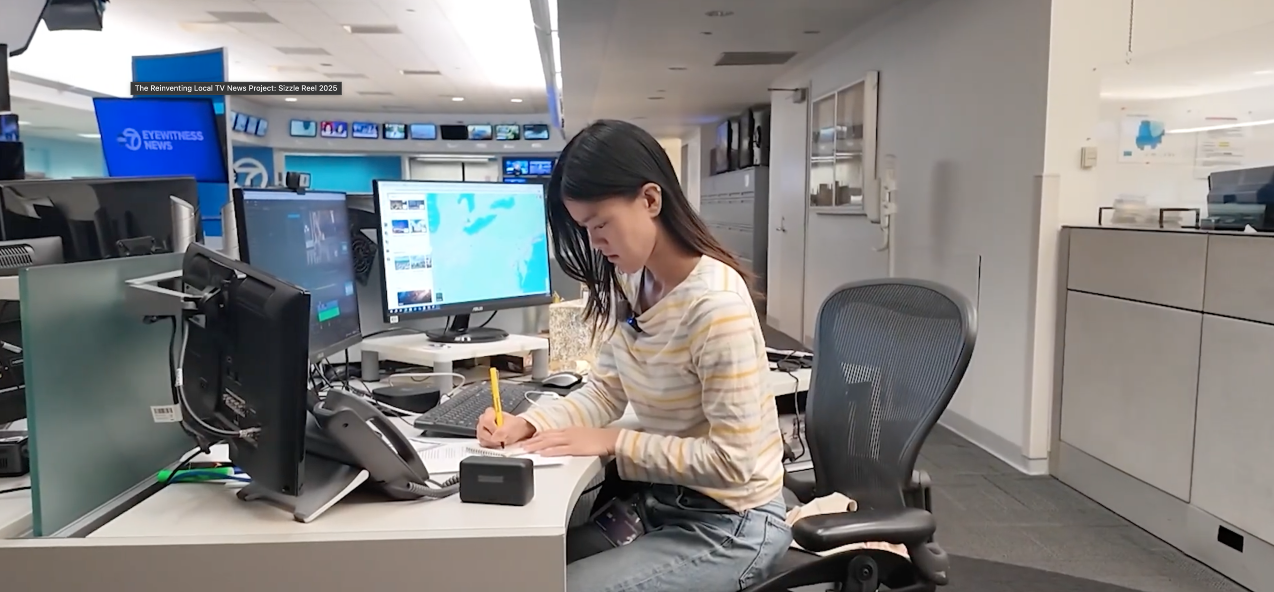 Photo shows woman in a newsroom writing at a desk